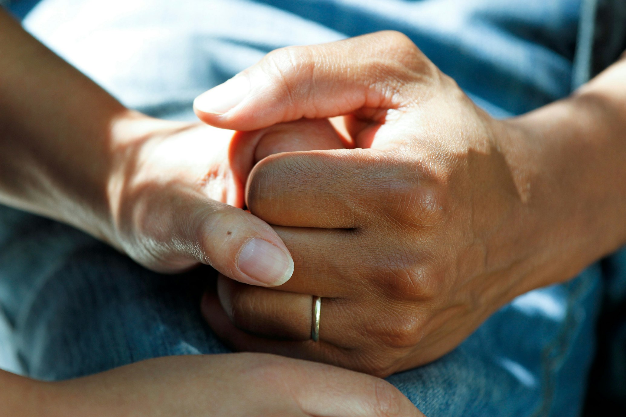 Close-up of two people's hands clasped together, one hand holding the other in support.