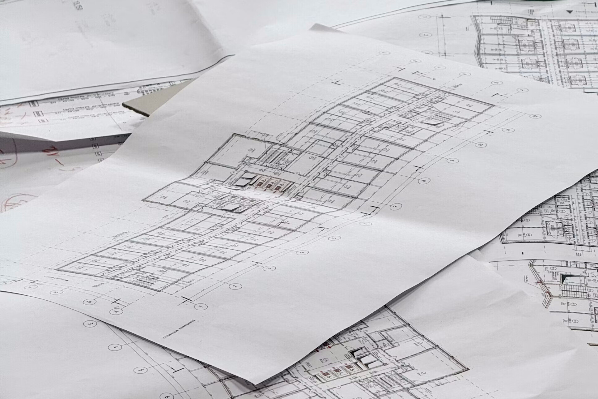 Layered architectural floor plans spread across a table, one drawing overlapping the next.