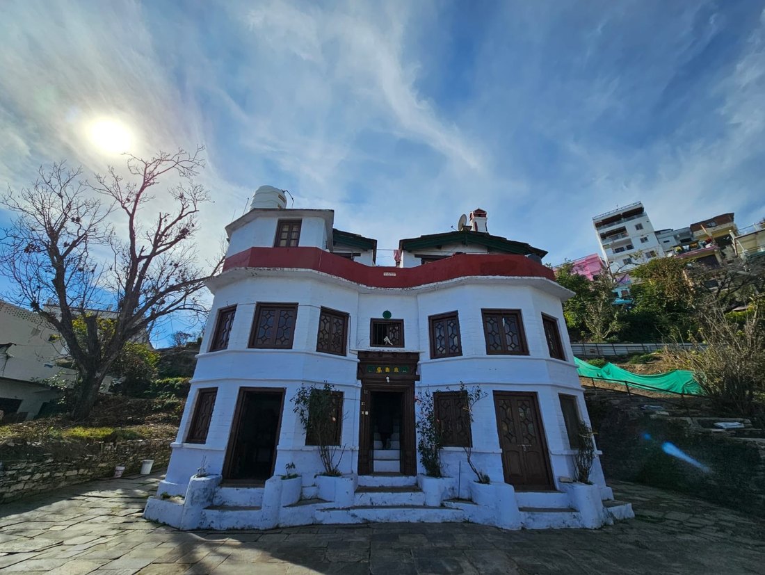 A white and red hundred-year-old house with curved balconies in Lala Bazar, Almora, under a bright sky.