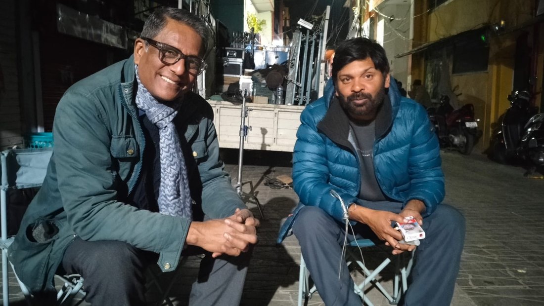 Two men seated on the Lala Bazar street in Almora at night, between shots, with film equipment behind them.